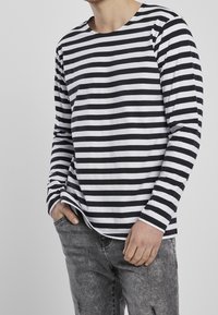 Camicia a maniche lunghe a righe bianche e nere con collo rotondo, dotata di una vestibilità rilassata e di un morbido tessuto in cotone, abbinata a jeans grigi.