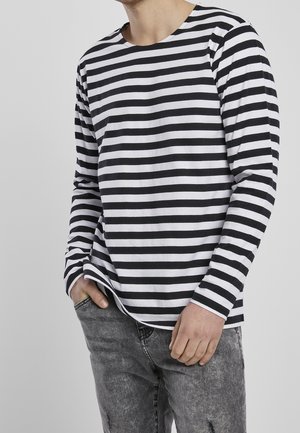 Chemise à rayures noires et blanches à manches longues avec un col rond, présentant une coupe décontractée et une texture en coton doux, associée à un jean gris.