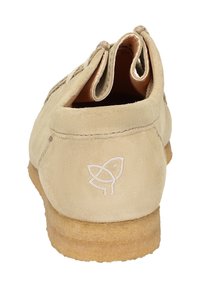 Beige Wildlederschuh mit runder Zehenpartie, ausgestattet mit einer Gummisohle und einem dezenten gestickten Logo an der Ferse. Entworfen mit zwei seitlichen Öffnungen.