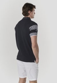 Polo nautique, corps bleu marine, manches contrastantes gris, col brodé, manches courtes, petit logo sur la manche, associé à un short blanc.