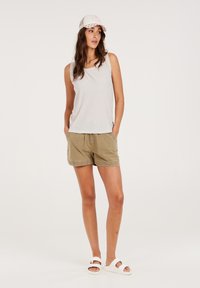 Hellgraues, geripptes Tanktop, khakifarbene Shorts mit Taschen und weiße Sandalen. Das Modell trägt eine weiße Kappe mit einem bedruckten Design.
