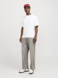 Hvid kortærmet t-shirt, grå baggy jeans og hvide sneakers med sorte accenter. En rød kasket med et logo fuldender outfittet.