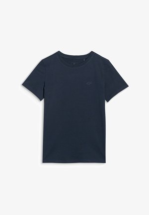 Jeune fille portant un t-shirt bleu marine, un pantalon large rose vif et des baskets blanches et violettes, debout devant un fond uni.