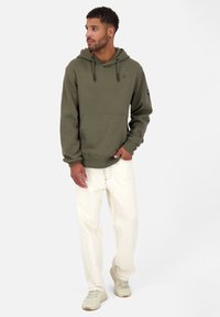 Olijfgroene hoodie van katoenmix met een voorkantoor, ribbelmanchetten en veters; gecombineerd met off-white denim en lichte sneakers.
