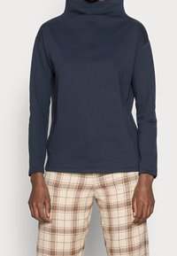 Top a manica lunga blu navy con colletto alto, realizzato in materiale morbido, caratterizzato da una vestibilità comoda e una texture liscia, abbinato a pantaloni a quadri.