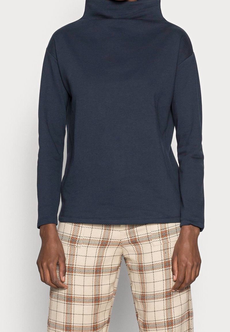 Top a manica lunga blu navy con colletto alto, realizzato in materiale morbido, caratterizzato da una vestibilità comoda e una texture liscia, abbinato a pantaloni a quadri.