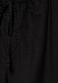 Pantalon en tissu noir avec une taille élastique, une poche latérale visible et un cordon de serrage.