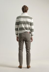 Camisa polo de manga larga a rayas en blanco y verde olivo combinada con pantalones gris claro y zapatos de ante marrón, vista desde la parte posterior.