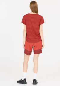 Rødstribet t-shirt med en afslappet pasform, parret med røde shorts med et farveblokdesign. Sorte sportssko og hvide sokker.