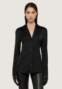 Blusa nera a maniche lunghe con colletto a punte, chiusura frontale con bottoni, texture liscia e silhouette aderente, abbinata a pantaloni neri lucidi.