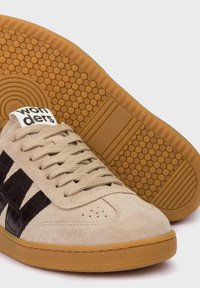 Zapatillas de ante beige con rayas de cuero negro, suela de goma texturizada y cordones beige. La etiqueta de la marca en la lengüeta dice "wonders."
