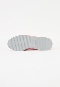 Semelle de basket rose avec une semelle extérieure en caoutchouc gris texturée, présentant des rainures horizontales et un design à bout arrondi. Marque visible sur la semelle.