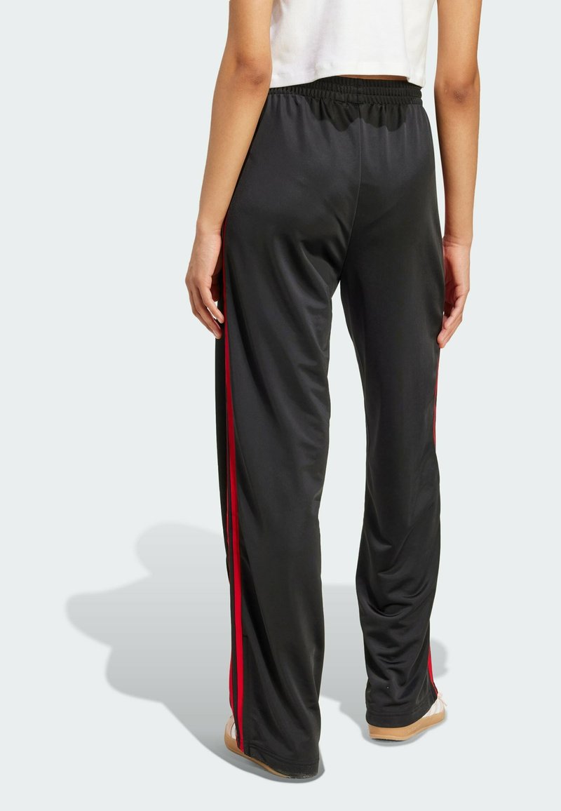 Pantalones deportivos negros de corte holgado, con franjas laterales rojas y una cintura elástica. Fabricados con un tejido suave y ligero.