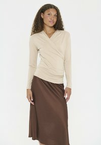 Beige långärmad omslagstopp med draperad detaljering, parat med en flödande brun midi-kjol som visar en jämn textur och en subtil glans.