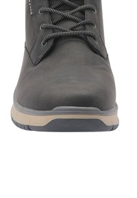 Priekšējais skats uz melnu ādas kurpi ar auklēm un bēgu un melnu zoli uz balta fona.