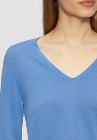 Helles blaues, v-ausschnitt gestricktes Sweatshirt mit langen Ärmeln. Weiche, glatte Textur mit einem dezenten, gerippten Muster entlang der Kanten.