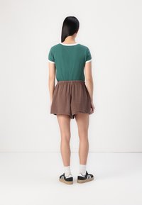 Green short-sleeve T-shirt with white trim, paired with brown textured shorts. Black sneakers with white socks complete the outfit.
