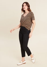 Leopardenprint top met korte mouwen en V-hals, gecombineerd met zwarte hoge taille broeken en witte instappers met gouden hardware accenten.