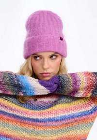 Ružová pletená čiapka s rebrovaným vzorom, nosená s viacfarebným pruhovaným sveterom s voľným strihom a okrúhlym výstrihom.