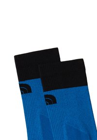 Blå strumpor med svarta ribbade manschetter, prydda med ett mönster av kontrasterande blå ränder och en svart logodetalj på sidan.