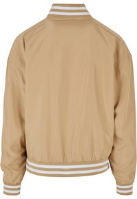 Giacca bomber beige chiaro con una texture liscia, colletto e polsini a coste bianchi a strisce e vita elastica. Il design sul retro è semplice.