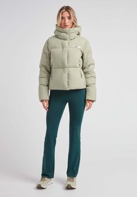 Lys grøn oppustelig jakke med en kasseformet design, høj krave og lynlåslommer. Kombineret med mørk teal leggings og lyse sneakers.