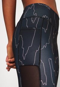 Leggings taille haute en tissu bleu foncé avec un motif linéaire abstrait blanc, accentués par des panneaux en maille sur les côtés.