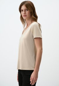 T-shirt beige a maniche corte con scollo a V, realizzato in un tessuto morbido, con una vestibilità comoda e dettagli di cucitura all'orlo e alle maniche.