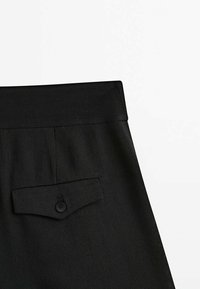 Pantaloni neri su misura con una finitura liscia, una vita alta e una tasca posteriore con chiusura a bottone.