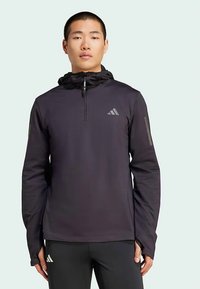 Musta urheiluhuppari, jossa on puolivetoketju edessä, säädettävä huppu, sileä pinta ja hillitty heijastava logo rinnassa ja hihoissa.