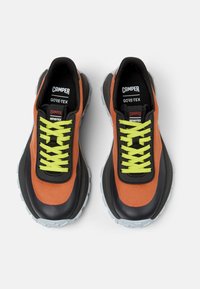 GORE-TEX sneakers with orange and black fabric upper, thick black sole, and bright green laces. Features padded tongue and logo accents.