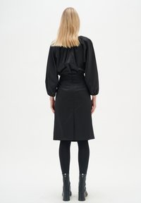 Musta pusero puffihihnoilla ja kustomoidut hameet, yhdistetty mustiin legginsseihin ja korkokenkiin. Sujuva pinta, minimalistinen muotoilu.