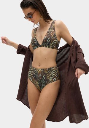 Kobieta w brązowym bikini w wzory i okularach przeciwsłonecznych, zakłada luźną, ciemnobrązową koszulę zapinaną na guziki.