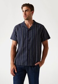 Camisa de manga corta en azul marino con franjas verticales amarillas y verdes, diseño con botones, hecha de tela ligera, corte relajado.