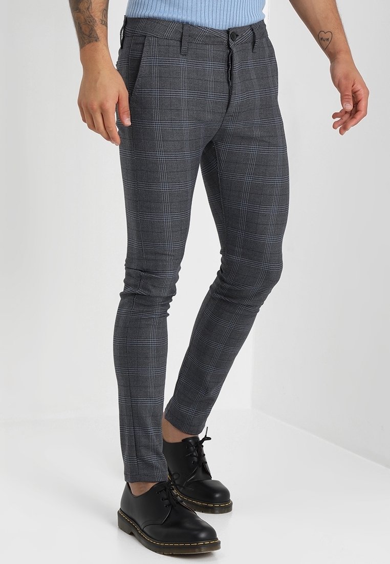 Šedé kostkované kalhoty slim fit s hladkou texturou, předními kapsami a knoflíkovým zapínáním. V kombinaci s černými šněrovacími botami.