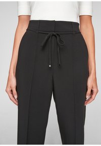 Pantalon noir avec taille à cordon de serrage, présentant un tissu texturé et une coupe ajustée. Fini lisse avec un léger éclat.