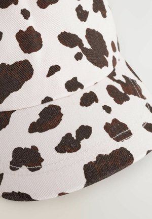 Casquette avec une base en tissu blanc et un design en imprimé vache marron ; forme structurée, accents surpiqués et visière courbée.
