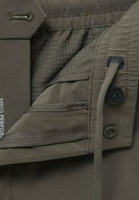 Intérieur de veste olive avec une texture lisse, plusieurs poches, une fermeture à bouton et un ourlet réglable avec cordon.