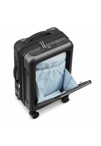 Valigia rigida nera con doppie ruote, dotata di una tasca frontale con zip rivestita in tessuto a righe blu e bianche. Meccanismo di chiusura visibile.