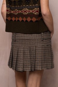 Isik, kes kannab pruuni mustriga kootud sviitrit ja pleeditud pruuni ja beeži houndstooth seelikut, seisab ühetaolise tausta ees.