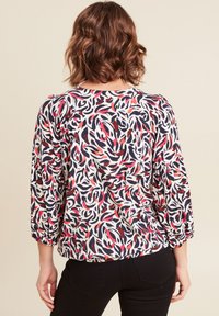 Blusa multicolore con un design fluido caratterizzato da motivi astratti in rosso, blu navy e bianco; presenta maniche a tre quarti e un orlo arrotondato.