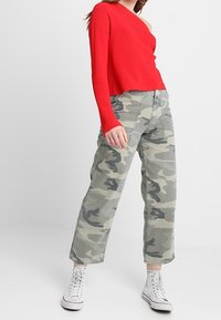 Rode geribde top met lange mouwen en een een-schouder ontwerp, gecombineerd met lichtgrijze camouflage wijde broek en witte hoge sneakers.