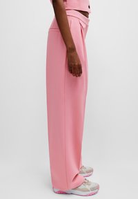 Pantaloni larghi rosa realizzati in tessuto morbido, con vita alta e tasche laterali, abbinati a sneakers grigie con dettagli rosa.