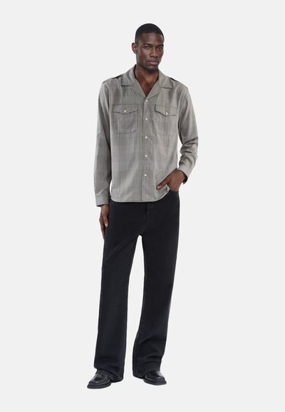 Camicia a quadri grigia con due tasche sul petto, abbinata a pantaloni ampi in velluto a coste neri e scarpe nere.