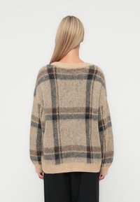Beige geruite sweater met een losse pasvorm, voorzien van zwarte en bruine strepen. Gebreide textuur en geribbelde zomen. Zacht, warm materiaal.
