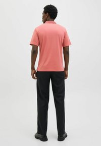 Világos korall színű polo póló, rövid ujjú és galléros, fekete nadrággal és fekete cipővel párosítva, hátulról bemutatva.