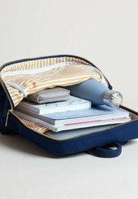 Zaino blu navy con fodera a righe gialle e bianche, contiene quaderni, una bottiglia d'acqua e una pochette grigia. Scomparto con zip.