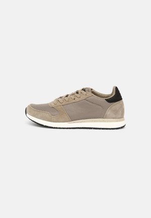 Zapatillas con una parte superior de gamuza y malla en color beige, talón texturizado en negro, plantilla blanca y suela de goma negra. Diseño clásico con cordones.