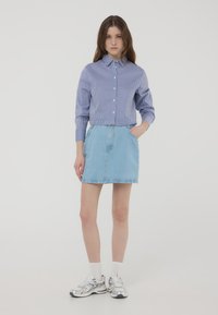 Camicia a maniche lunghe con righe blu e bianche, abbinata a una gonna di jeans chiara. L'outfit include sneakers argentate e calzini bianchi.