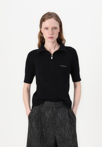 Polo negru cu model în relief, cu mâneci scurte și guler cu fermoar, featuring branding minim și un finisaj texturat.